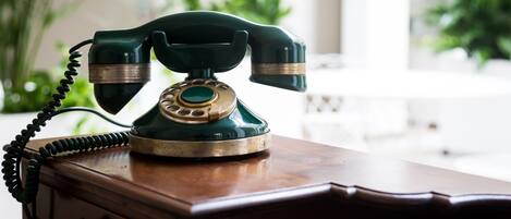 Un teléfono antiguo verde con dial giratorio sobre un escritorio de madera.