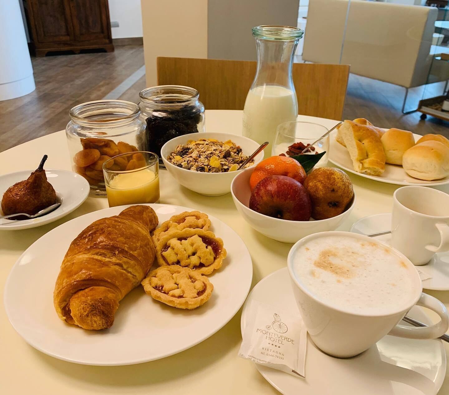 Desayuno con cruasanes, fruta, cereales y café sobre una mesa.