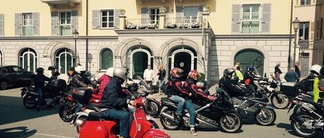 A group of motorcyclists parked in front of a building with balconies and arched windows.