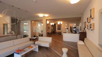 A spacious living area with a white sofa, a coffee table with books, and a kitchen area in the background.