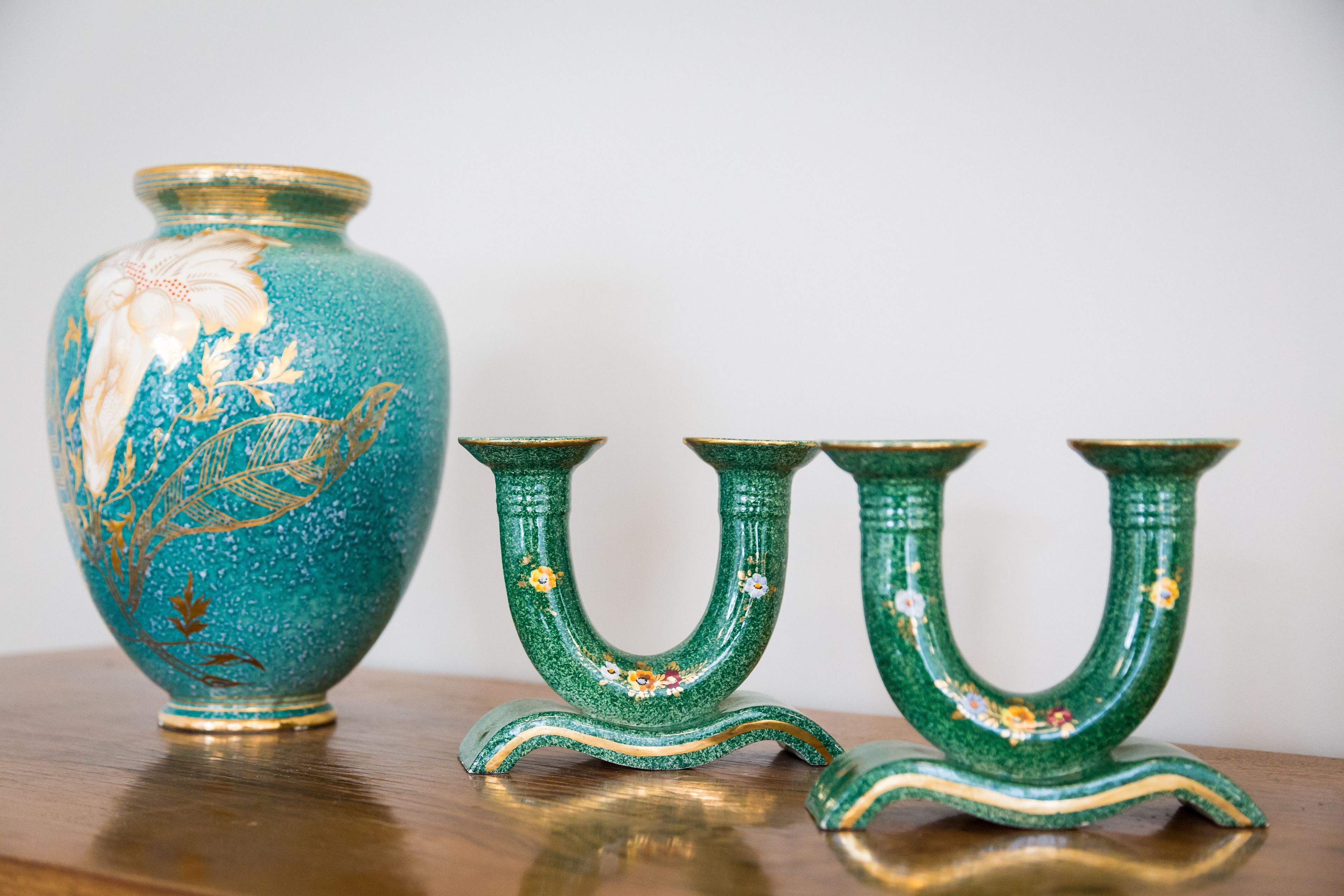 A teal vase with floral designs and three matching candle holders on a wooden surface.