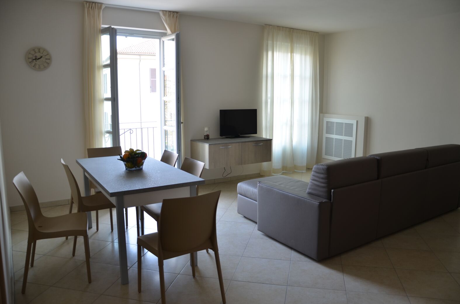 A living room with a dining table, chairs, a sofa, a TV, and a window with curtains.