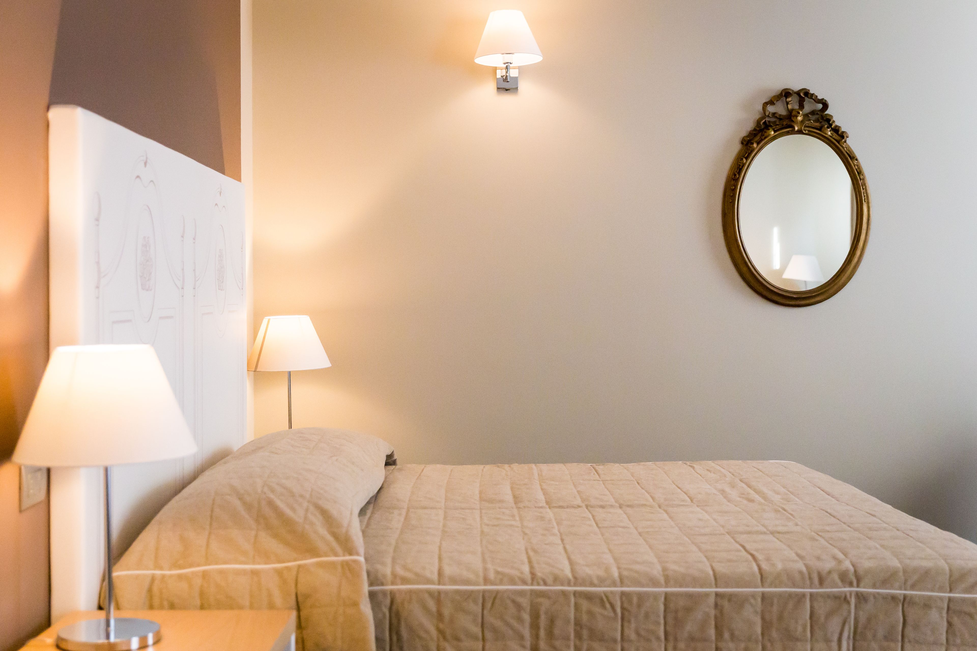 Ein ordentlich bezogenes Bett mit einer gesteppten Decke, zwei Nachttischlampen, einem wandmontierten Spiegel und einem gerahmten Bild an der Wand.