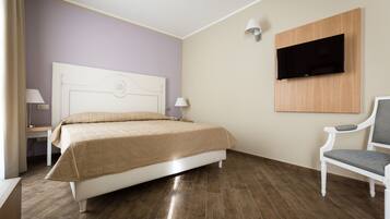 A bedroom with a bed, a chair, a TV mounted on the wall, and a nightstand with a lamp.