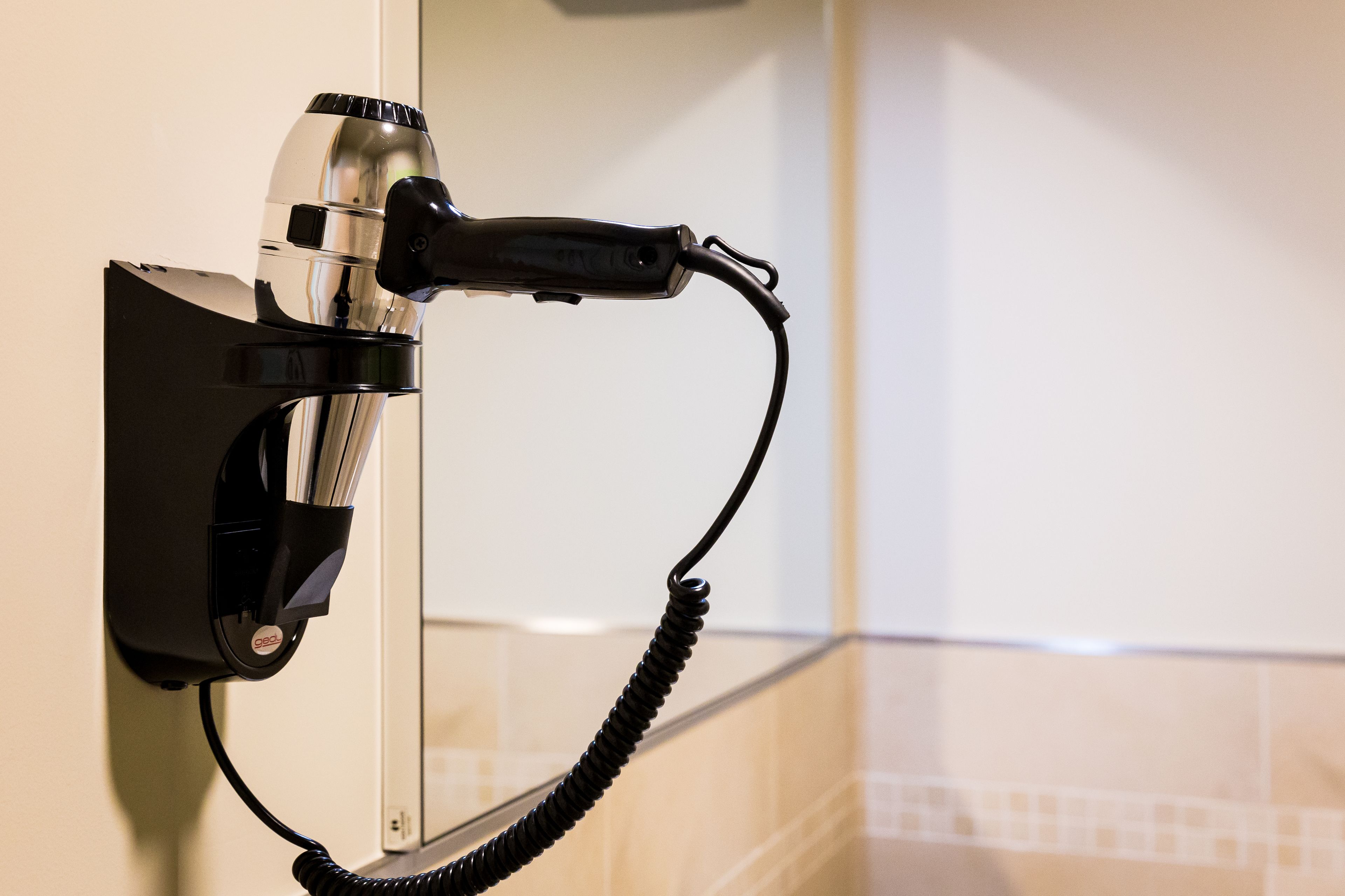 A hair dryer mounted on a wall with a coiled cord.