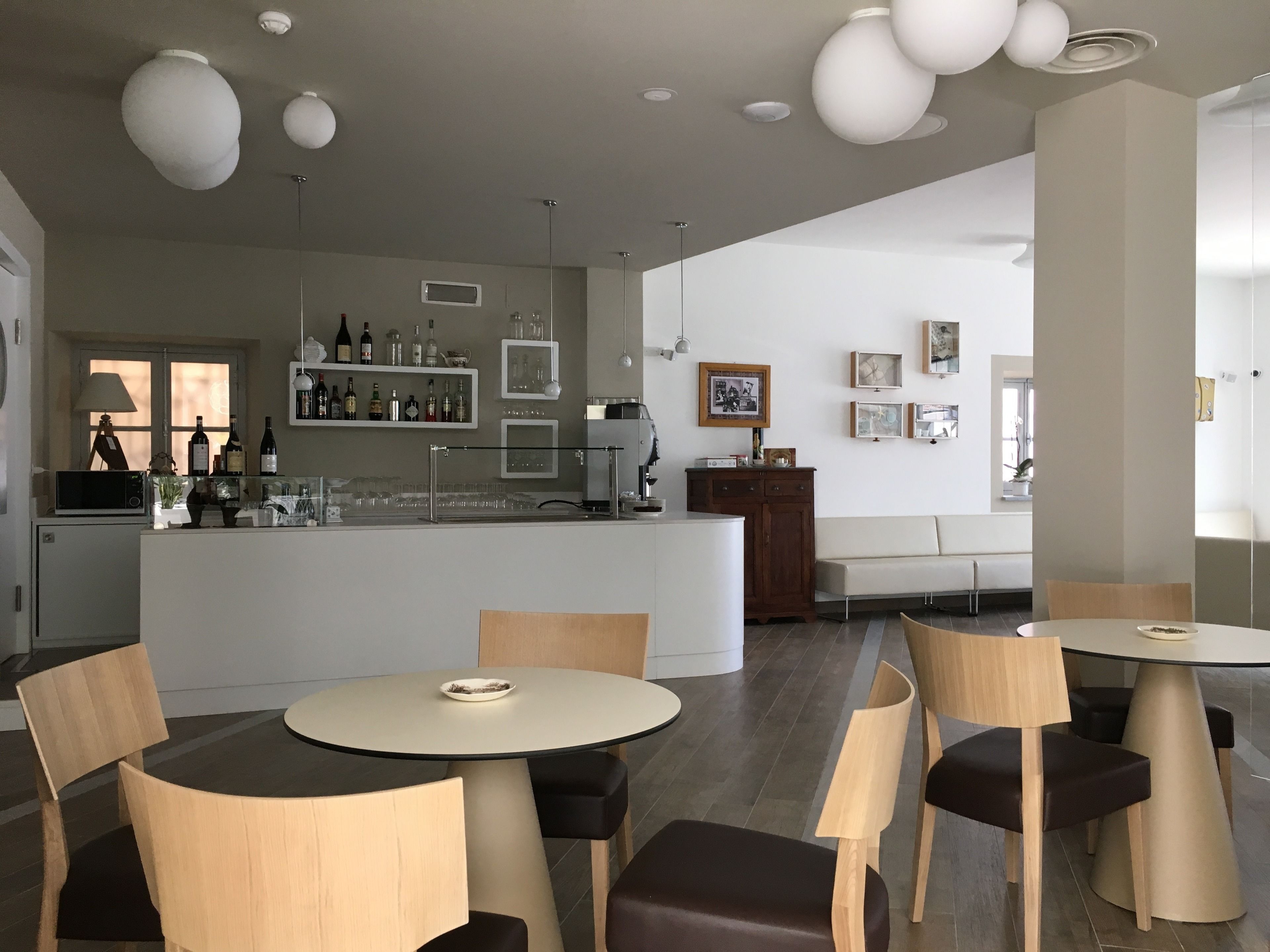 Een modern restaurantinterieur met ronde tafels, houten stoelen, een bar met flessen en een zithoek met een bank en stoelen.