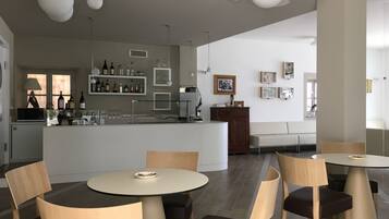 Een modern restaurantinterieur met ronde tafels, houten stoelen, een bar met flessen en een zithoek met een bank en stoelen.