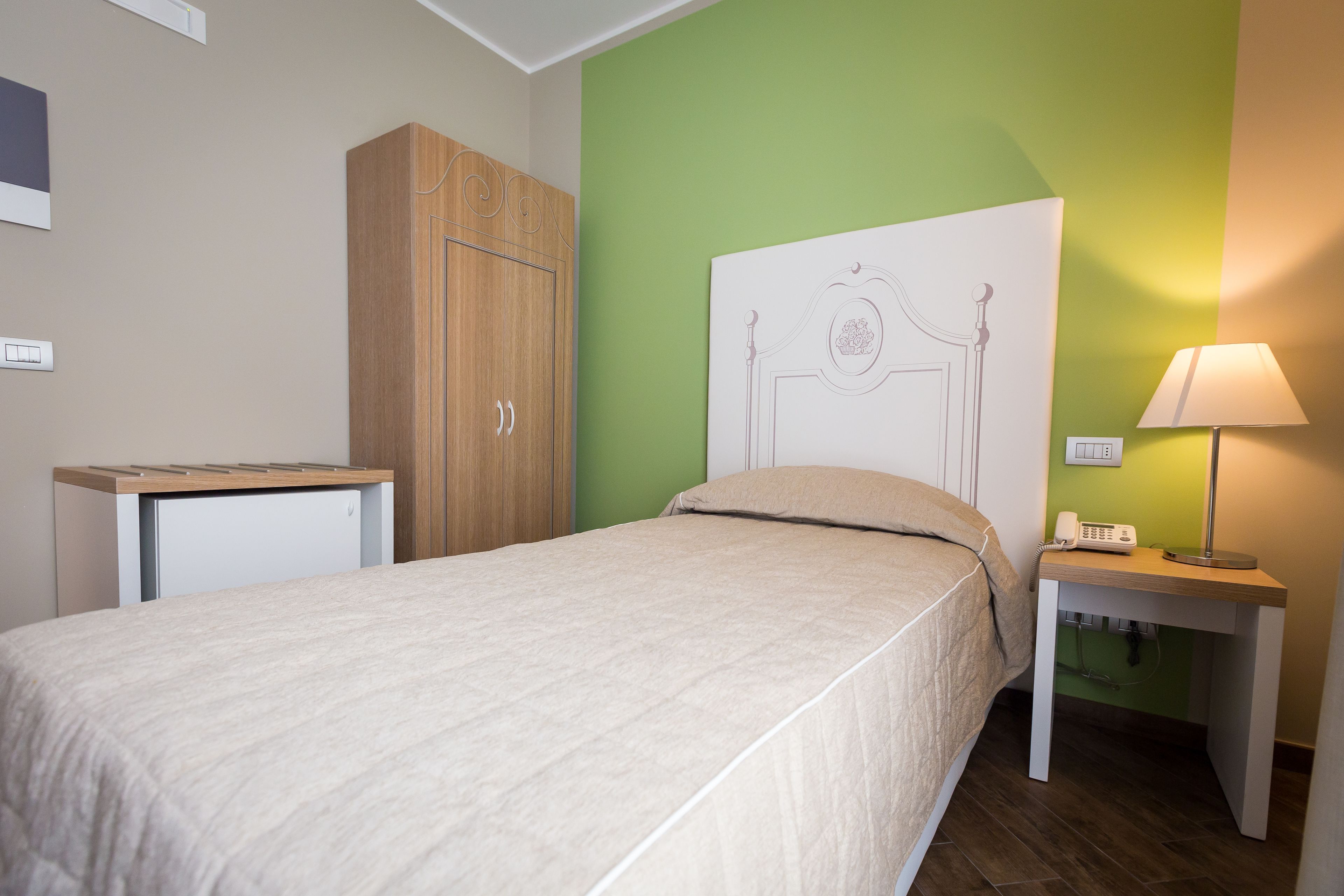 Una camera da letto con un letto, un armadio in legno, un comodino con una lampada e un telefono fissato al muro.