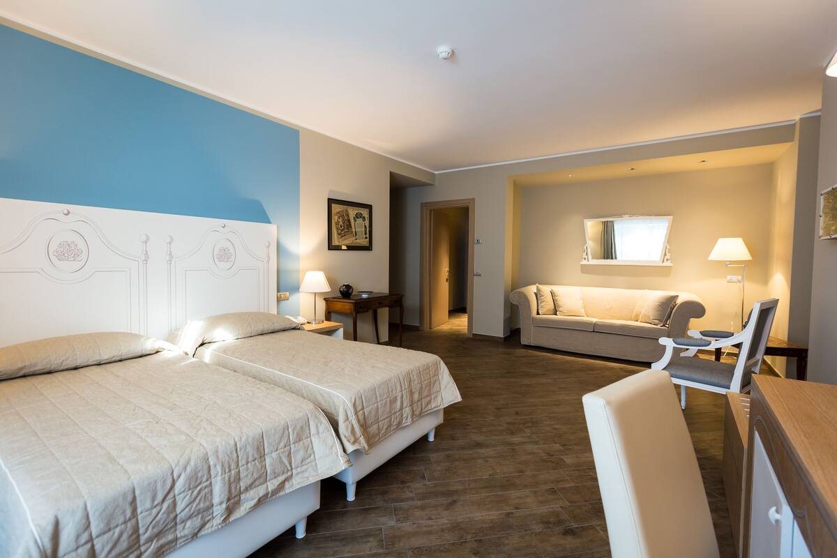 A hotel room with two beds, a sofa, a chair, a desk, and a small table.