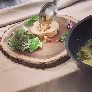 A wooden serving board with a piece of food, garnished with greens and flowers, on a table.