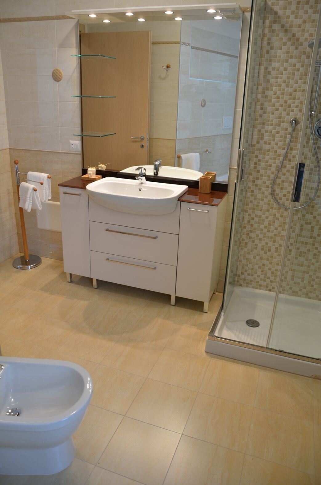 A modern bathroom with a double sink, a glass shower enclosure, and a bidet.