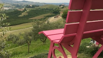 A red chair on a grassy hill overlooking a vineyard and rolling hills.