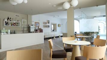 Un restaurant moderne doté d’un bar, de différents types de tables et de chaises, ainsi que d’une grande fenêtre laissant entrer la lumière naturelle.