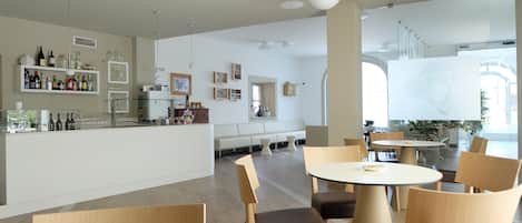 A modern restaurant with a bar area, seating arrangements, and a large window providing natural light.