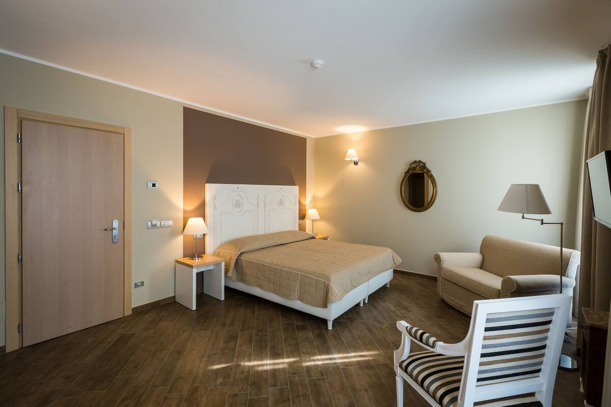 A hotel room with a bed, bedside tables, a chair, a sofa, and a television.