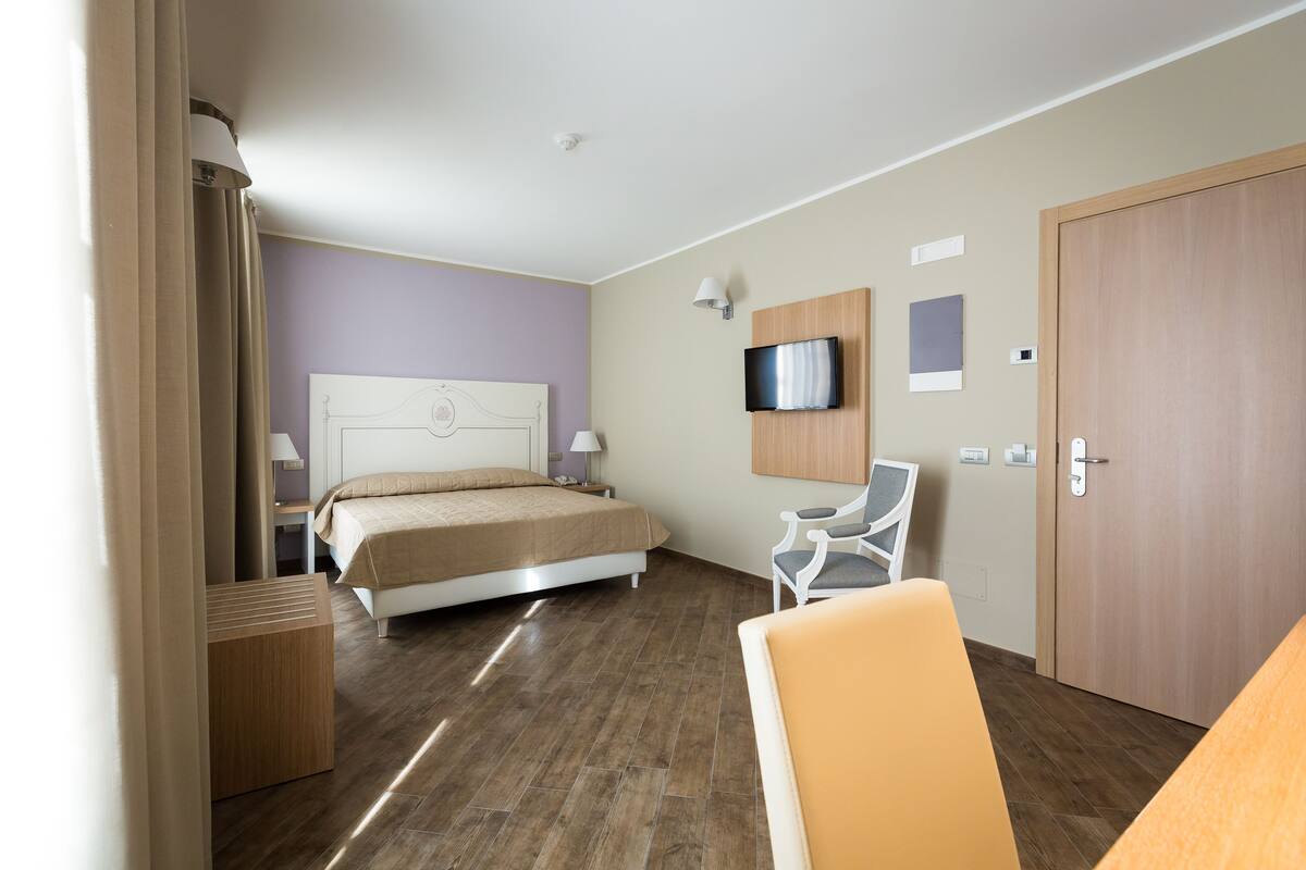 A hotel room with a bed, a TV mounted on the wall, a desk, and a chair.