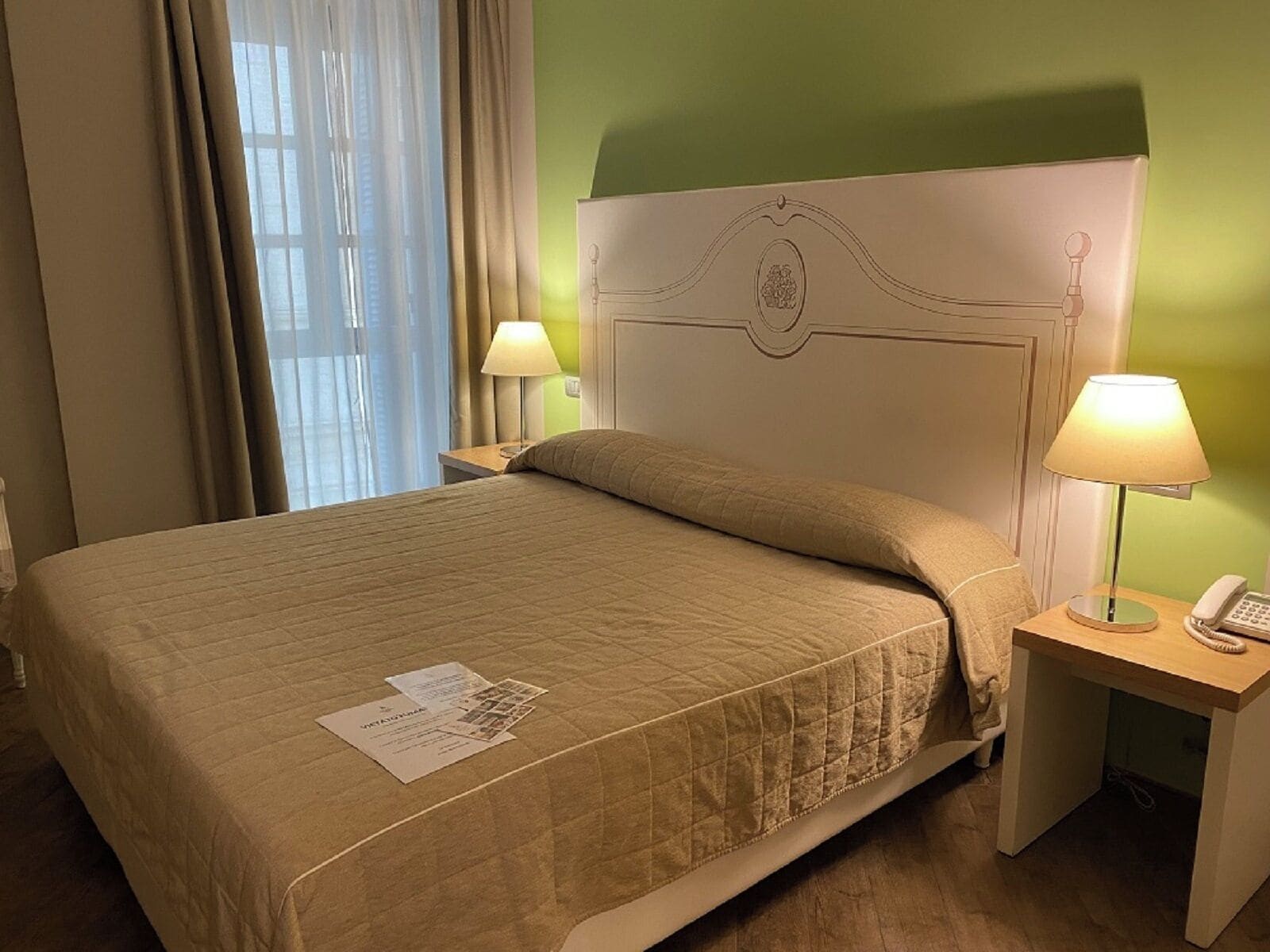 Une chambre d’hôtel avec un lit, deux lampes de chevet, une table de chevet avec un téléphone et une fenêtre avec des rideaux.