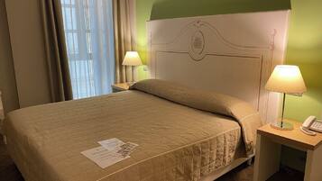 Une chambre d’hôtel avec un lit, deux lampes de chevet, une table de chevet avec un téléphone et une fenêtre avec des rideaux.