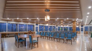 A spacious dining area with wooden tables and blue chairs, large windows, and a modern ceiling design.