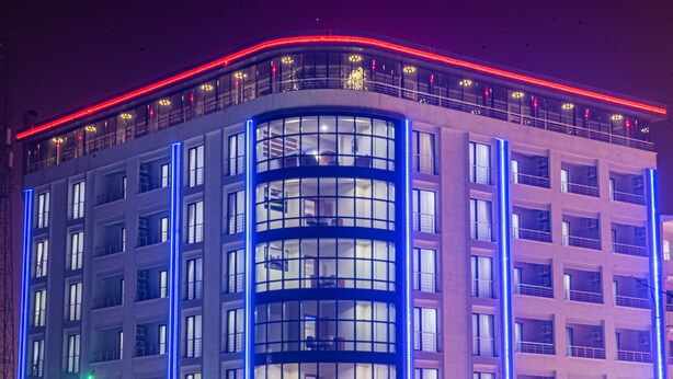 A multi-story hotel with a curved facade, large windows, and illuminated red and blue neon lights.