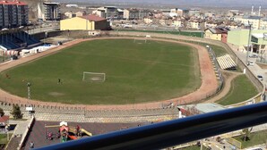 A stadium with a large field, seating areas, and a view of mountains in the background.