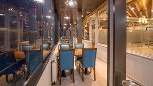 A modern dining area with glass partitions, wooden tables, and blue chairs.