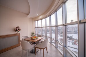 A dining area with a table set for two, a decorative vase, and a view of a snowy landscape through large windows.