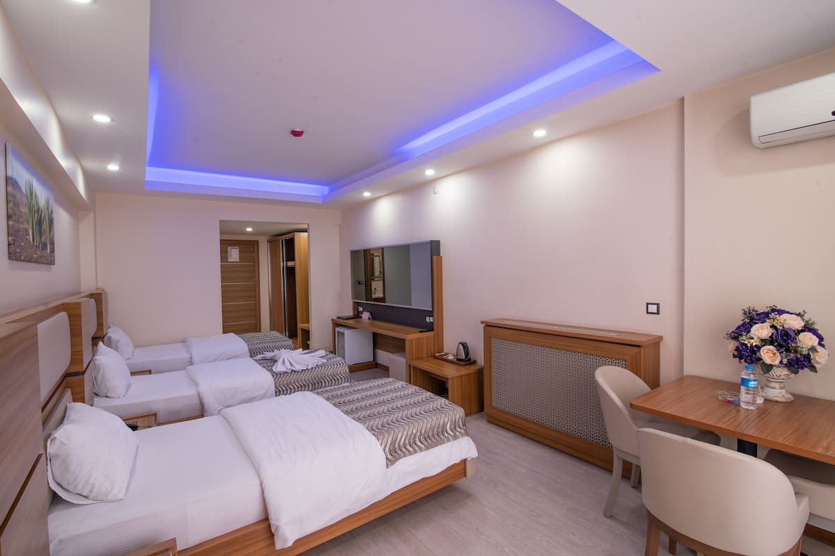 A hotel room with two single beds, a desk, a chair, a television, and a small table with a vase of flowers.