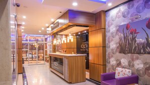 A hotel reception area with a wooden reception desk, a purple sofa, and a wall with a floral mural.
