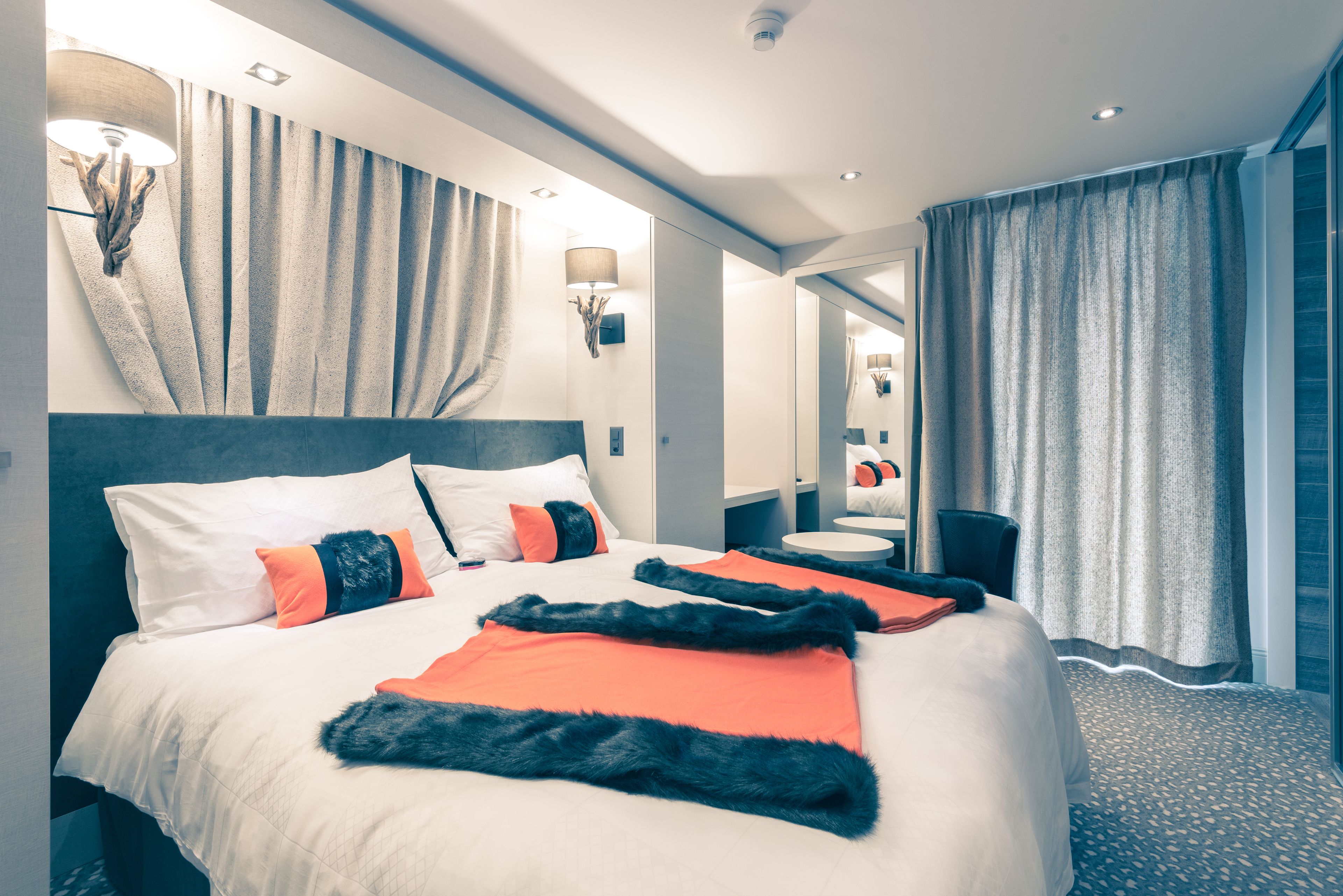 Une chambre d’hôtel moderne avec un grand lit, un miroir rond et un coin salon.