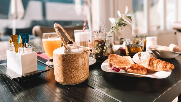 Une table de petit-déjeuner avec des croissants, des tartines et un verre de jus d’orange.