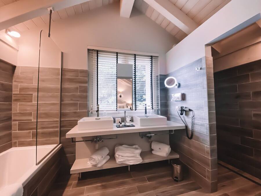 A modern bathroom with a large mirror, two sinks, a bathtub, and a vanity with towels.