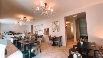 A modern hotel lobby with a dining area, a reception desk, and a staircase leading to the upper floors.