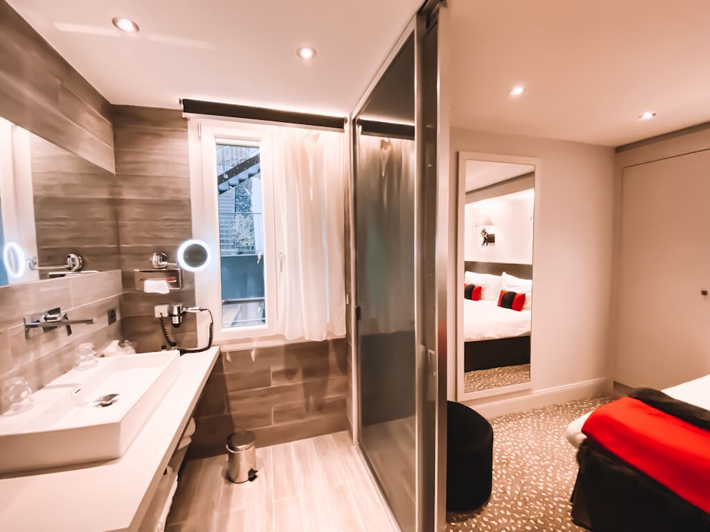 A modern hotel bathroom with a large mirror, a sink, and a shower area.