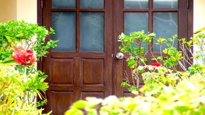 A wooden door with glass panels, surrounded by lush greenery and a red flower. - Palm Garden Resort Khaolak (Takua Pa)