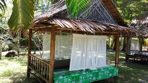 A thatched-roof hut with a bed covered by a white sheet, surrounded by greenery. - Palm Garden Resort Khaolak (Takua Pa)