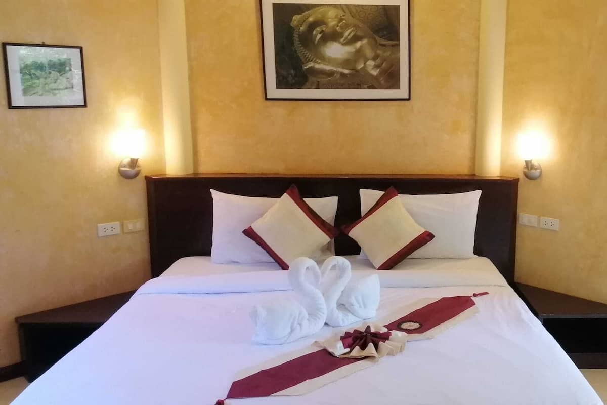 A hotel room with a neatly made bed, two wall-mounted lamps, and a framed artwork above the bed.