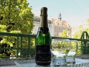 A bottle of Bohemia Seck Brut champagne and two glasses on a tray with a view of a bridge and buildings in the background. - Hotel Meran (Prague)