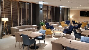 A modern hotel lobby with seating areas, tables, and a TV screen.