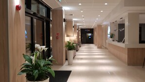 A hotel corridor with a reception desk, potted plants, and a modern interior design.