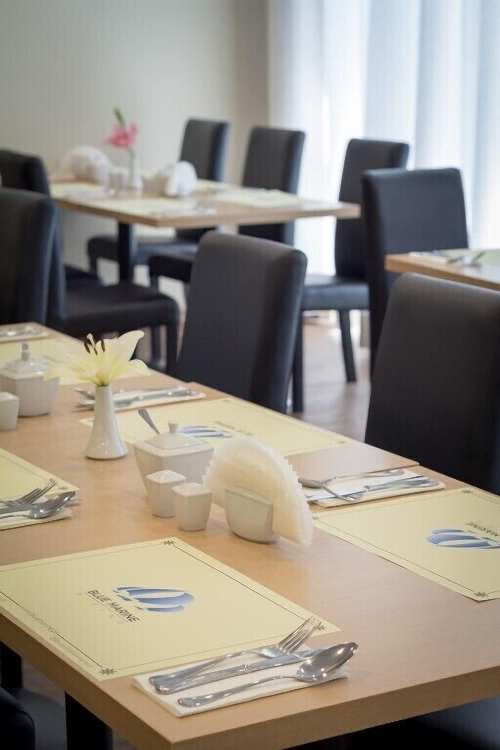 A dining area with tables set for a meal, including cutlery, napkins, and a vase with flowers.