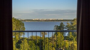 A view from a balcony overlooking a lake with trees and buildings in the distance.