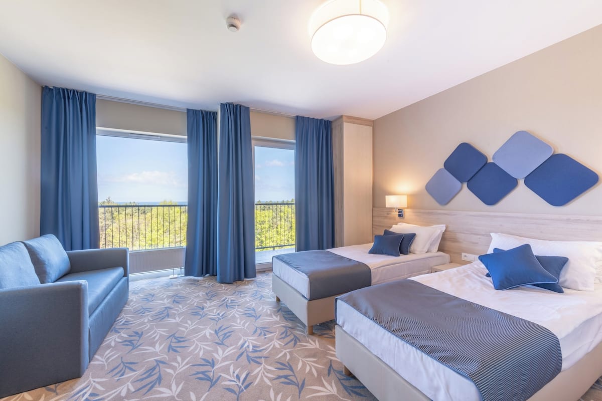 Ein Hotelzimmer mit Balkon, zwei Betten, einer Couch und einem gemusterten Teppich.