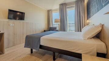 A hotel room with a bed, a TV mounted on the wall, a window with curtains, and a view of the outdoors.