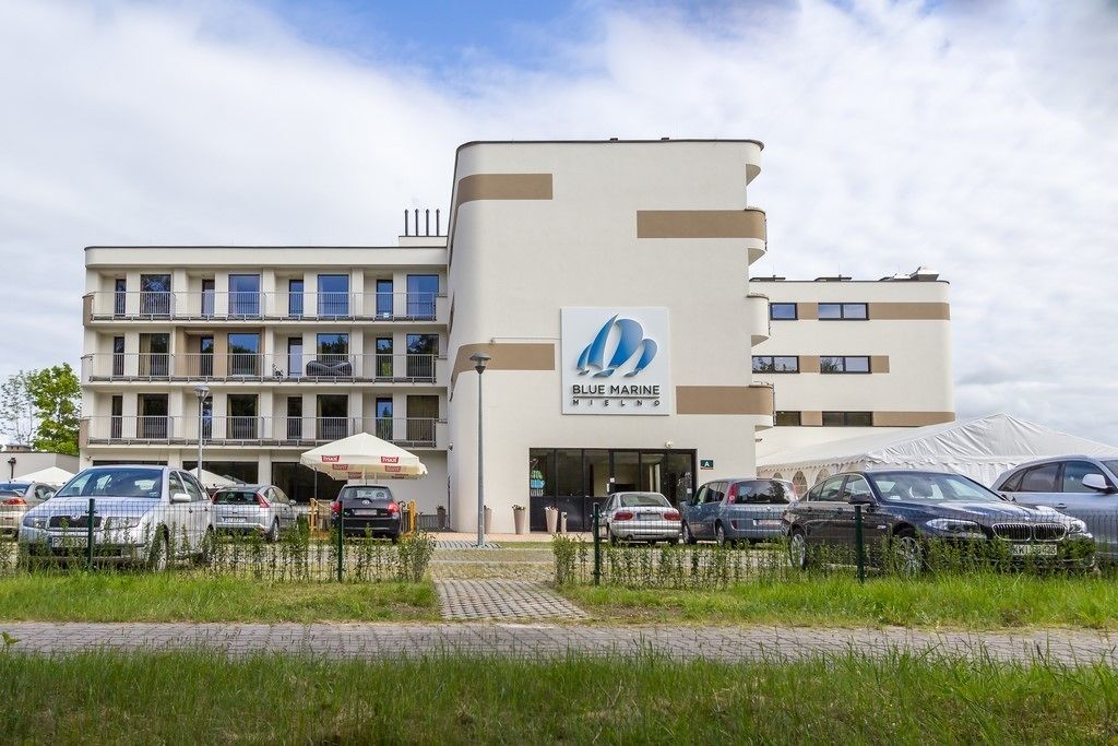 A modern building with a prominent Blue Marine logo, featuring multiple floors and a parking area with several cars.