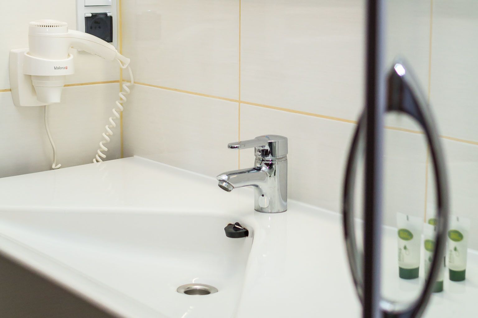 A bathroom with a white sink, a chrome faucet, and a hairdryer on a wall-mounted station.