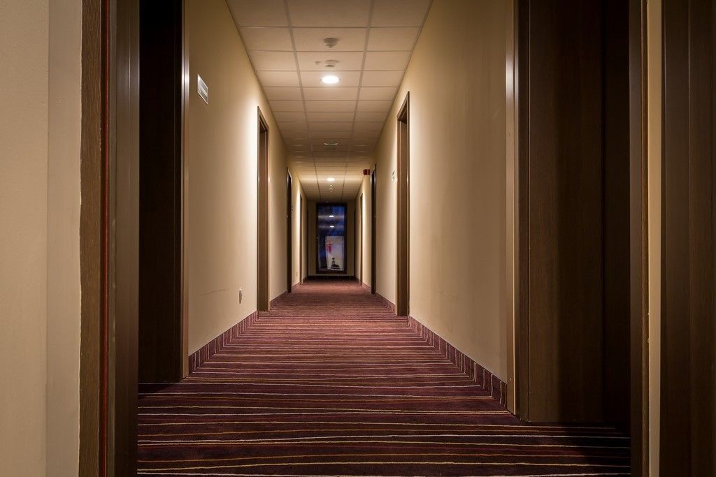 A hotel hallway with carpeted stairs, a ceiling with recessed lighting, and doors on both sides.