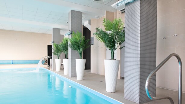 A swimming pool with clear blue water, surrounded by beige tiled walls and white pillars.
