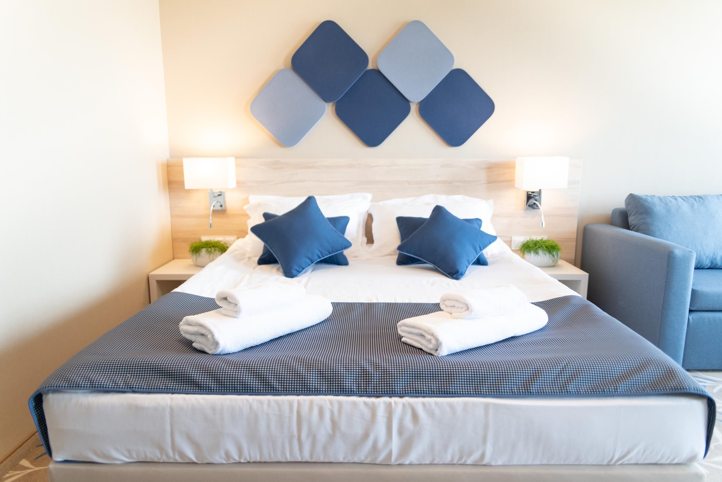 Un lit bien fait, avec une literie bleue et blanche, deux lampes de chevet et un élément décoratif mural au-dessus du lit.