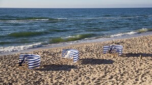 A beach with three striped beach chairs and umbrellas, a sandy beach, and the ocean.
